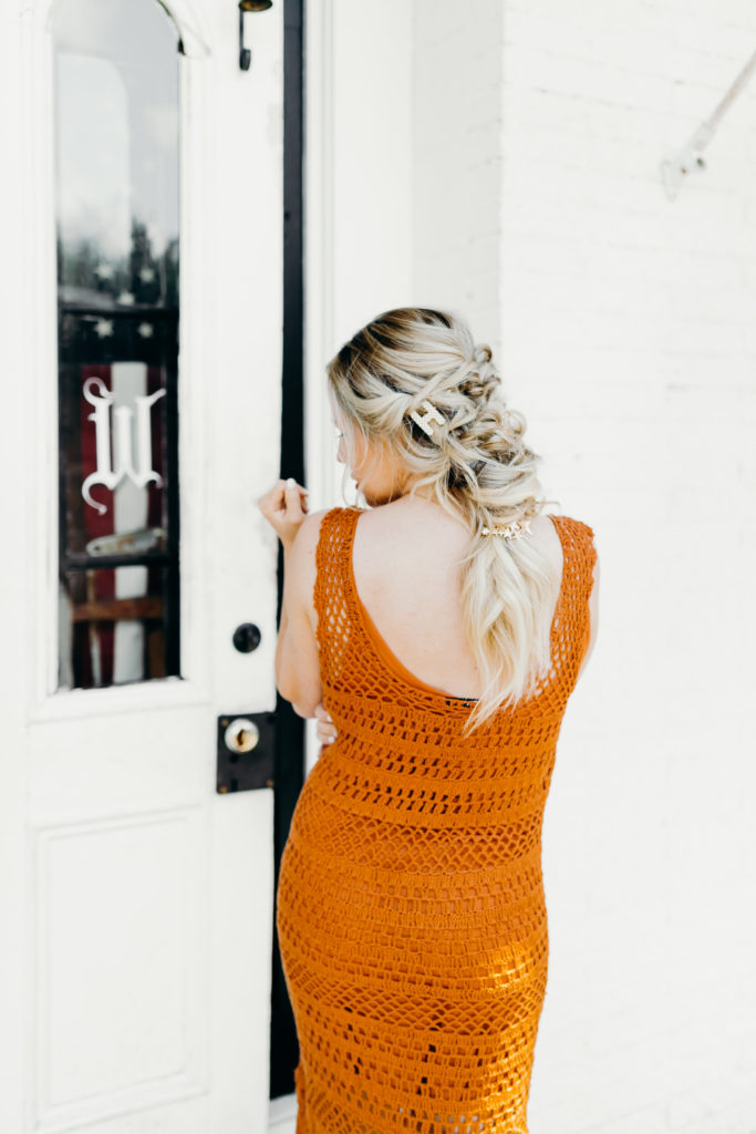 How to Wear Hair Clips by popular Nashville fashion blog, Nashville Wifestyles: image of a woman with a braided hairstyle and wearing a pearl letter H hair clip, gold bobby pins, and a star hair clip in her hair along with an orange crocheted maxi dress with fringe.