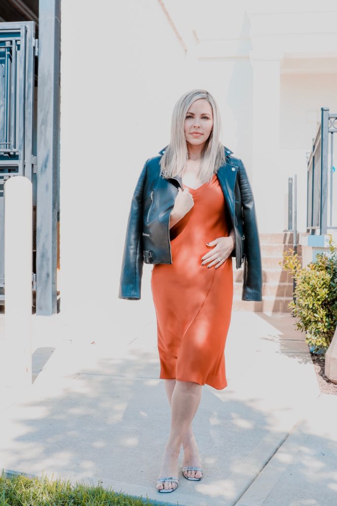 Edgy Date Night Look by popular Nashville mom fashion blog, Nashville Wifestyles: image of a woman wearing a leather jacket, rust colored satin midi dress, and heel sandals. 