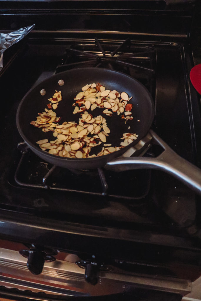 Honey Roasted Brussel Sprouts by popular Nashville life and style blog, Nashville Wifestyles: image of roasted slivered almonds on a black pan on a stove top.