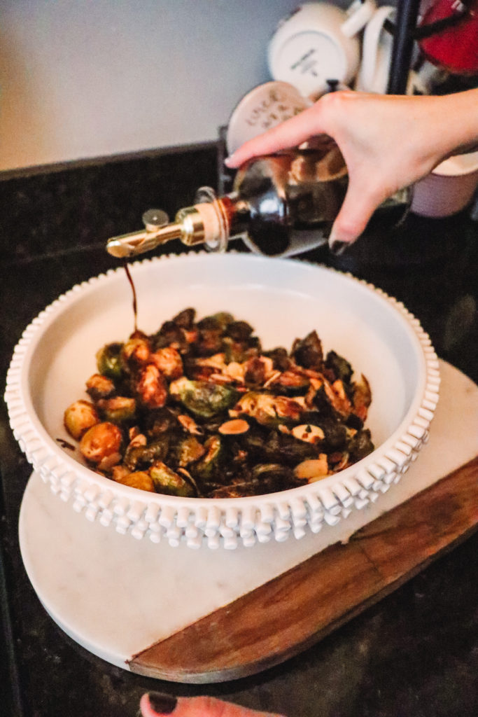 Honey Roasted Brussel Sprouts by popular Nashville life and style blog, Nashville Wifestyles: image of a woman drizzling balsamic vinegar on honey roasted Brussel sprouts.
