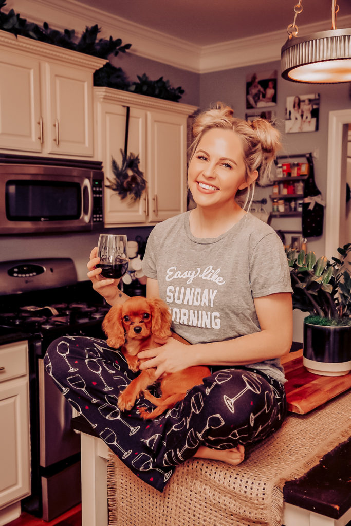 Pet Parent by popular Nashville lifestyle blog, Nashville Wifestyles:  image of a woman wearing loungewear and sitting on her kitchen counter while she holds her dog in her lap and a glass of wine in her hand.
