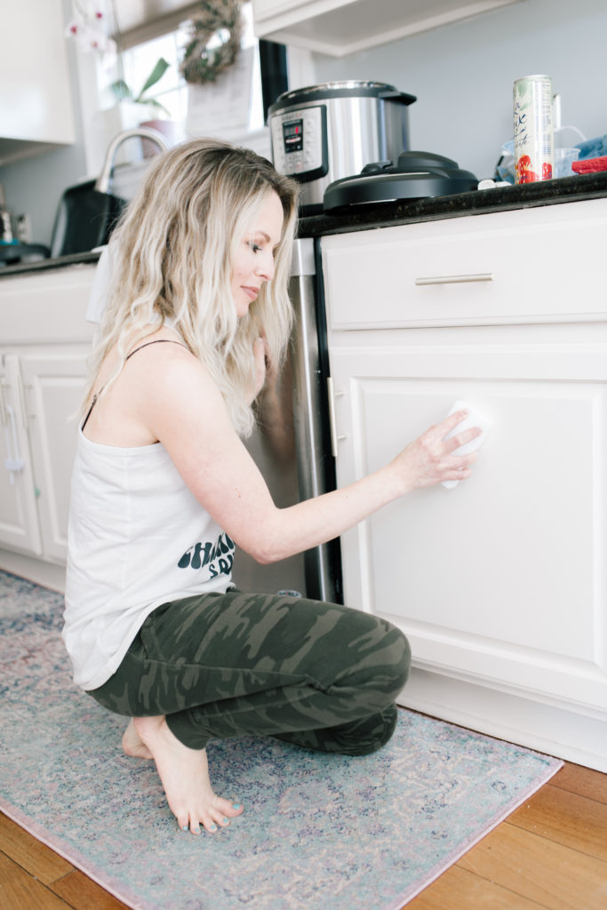 Spring Cleaning Simplified by popular Nashville lifestyle blog, Nashville Wifestyles: image of a woman whipping down her white kitchen cupboards. 