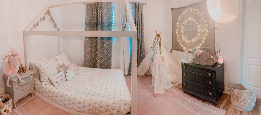 Toddler Floor Bed by popular Nashville motherhood blog, Nashville Wifestyles:  image of a room with a white house frame toddler floor bed, pink area rug, black dresser, fabric tee pee, moon light, grey dresser, gold and white bedding, grey and white stars drapes, and a rope basket. 