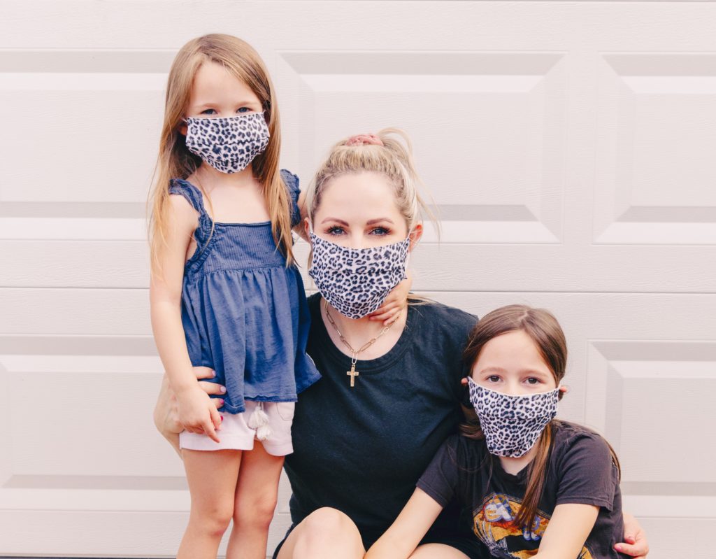 Life Transitions by popular Nashville lifestyle blog, Nashville Wifestyles: image of a mom and her two daughter sitting together in front of their garage door and wearing leopard print face masks. 