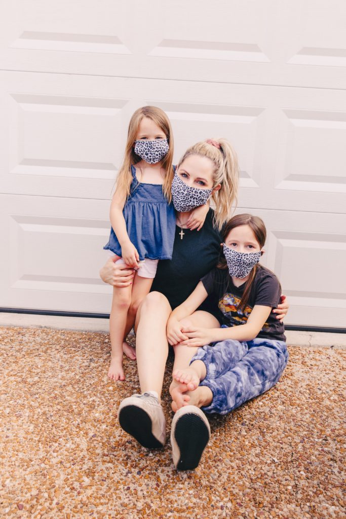 Life Transitions by popular Nashville lifestyle blog, Nashville Wifestyles: image of a mom and her two daughter sitting together in front of their garage door and wearing face masks. 