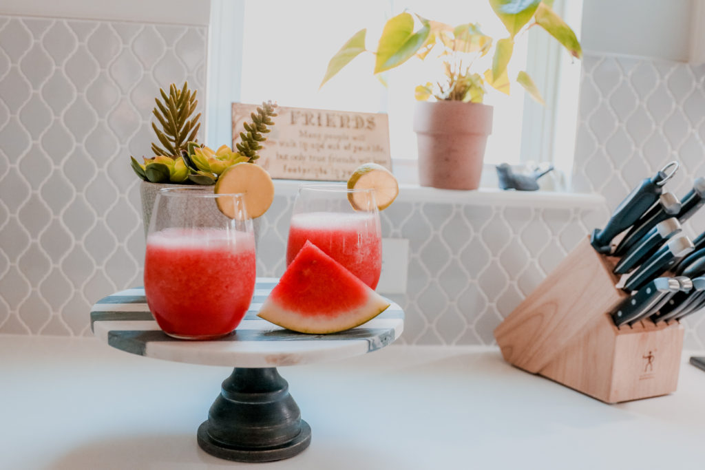 Watermelon Margarita by popular Nashville lifestyle blog, Nashville Wifestyles: image of watermelon margarita in a stemless wine glasses on a cake stand next to a slice of watermelon. 