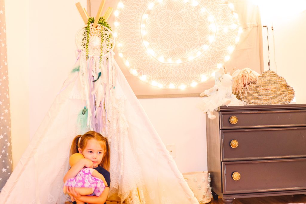 Toddler Room by popular Nashville motherhood blog, Nashville Wifestyles: image of a toddler girl sitting in a Etsy BenderBeeCompany Lace Teepee that's next to a Pottery Barn Teen Fairy Light Mandala Tapestry.