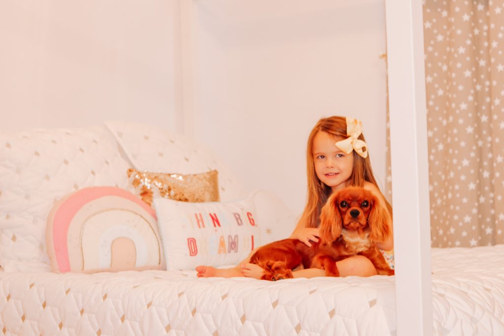 Benefits of Owning a Pet by popular Nashville lifestyle blog, Nashville Wifestyles: image of a young girl sitting on her bed and holding her dog in her lap. 