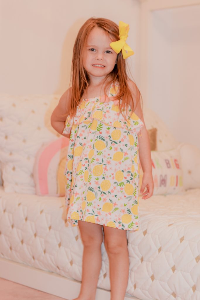 Toddler Room by popular Nashville motherhood blog, Nashville Wifestyles: image of a little girl wearing a lemon print dress and standing next to a Pottery Barn Kids Camden House Bed.