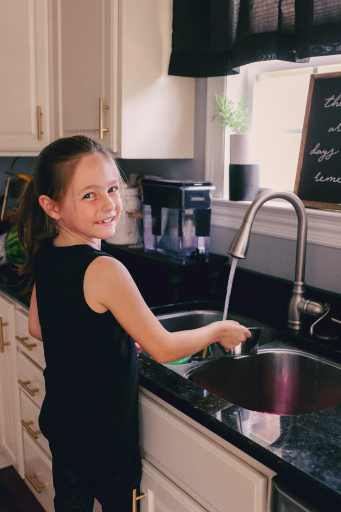 Chores for Kids by popular Nashville motherhood blog, Nashville Wifestyles: image of a young girl washing dishes at the sink. 