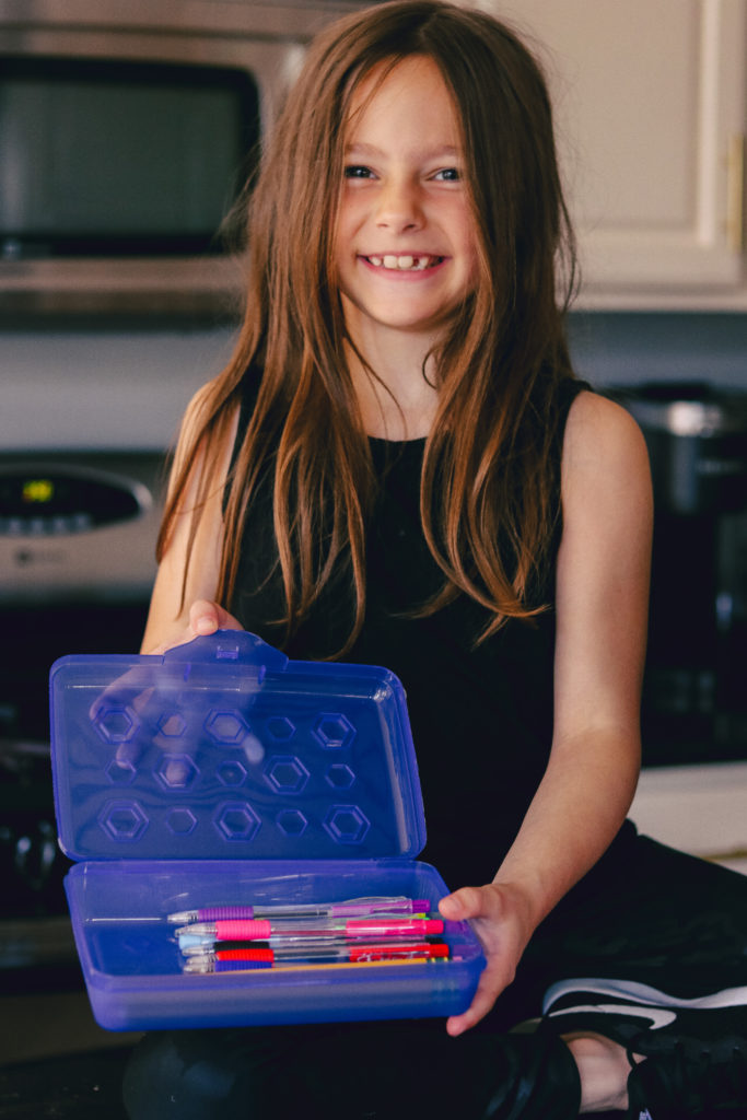 Back to School Tips by popular Nashville lifestyle blog, Nashville Wifestyles: image of a girl holding a Dollar General pencil box. 