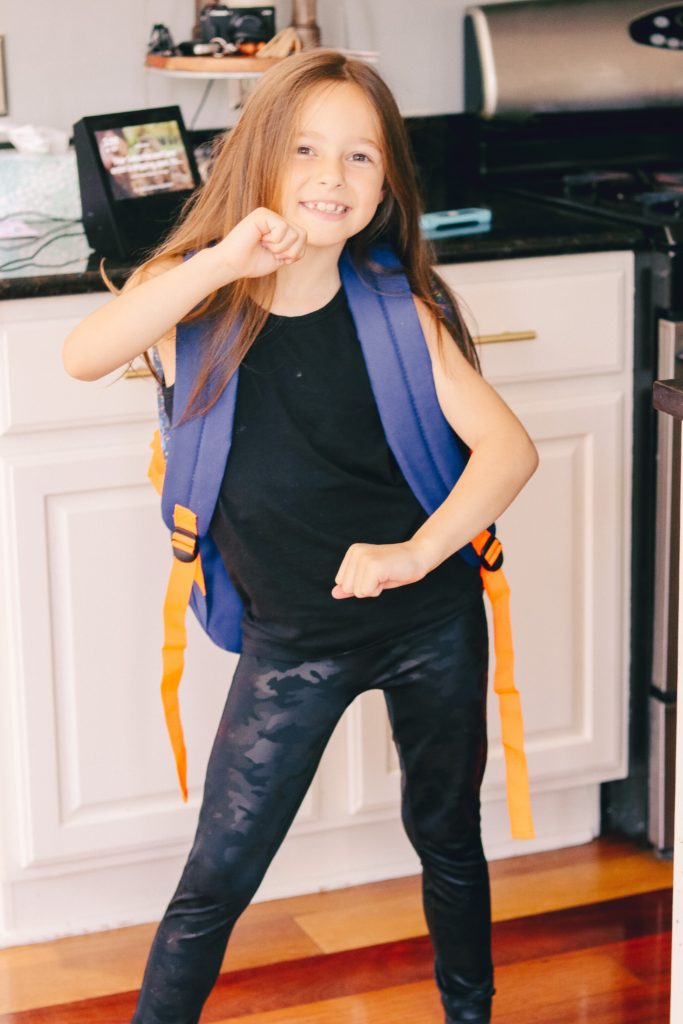 Back to School Tips by popular Nashville lifestyle blog, Nashville Wifestyles: image of a girl standing in her kitchen and wearing a Dollar General backpack. 