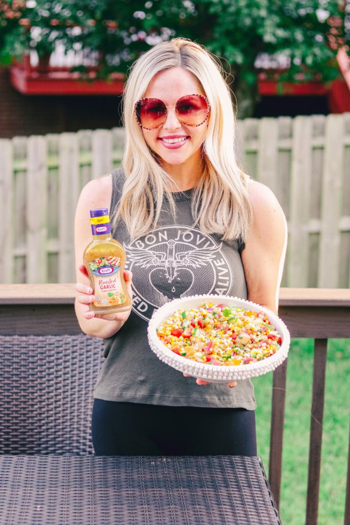 Summer Corn Salad Recipe by popular Nashville lifestyle blog, Nashville Wifestyles: image of a woman holding a bottle of Kraft roasted garlic vinaigrette and a bowl of summer corn salad.  