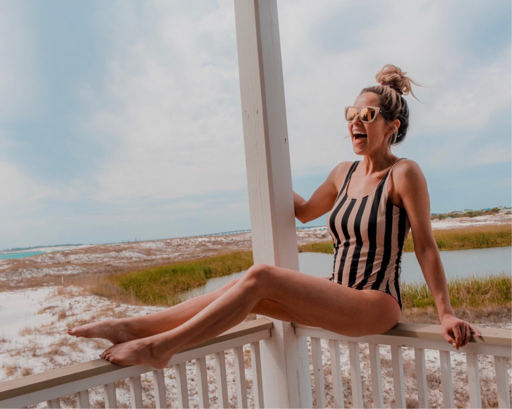 Travel Tips by popular Nashville travel blog, Nashville Wifestyles: image of a woman sitting on a balcony railing and wearing a tan and black strip swimsuit. 
