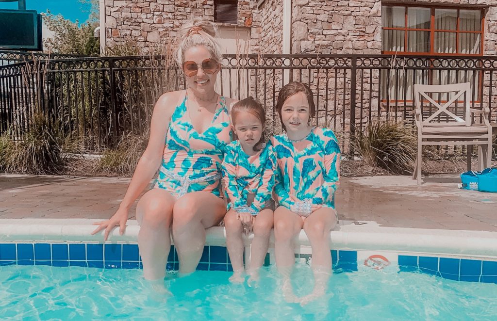 Pigeon Forge TN by popular Nashville travel blog, Nashville Wifestyles: image of a mom and her two young daughters wearing matching swimming suits and sitting on the edge of a swimming pool. 