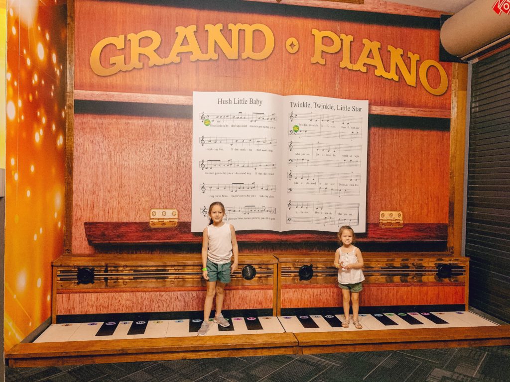 Pigeon Forge TN by popular Nashville travel blog, Nashville Wifestyles: image of two young girls standing on a interactive grand piano at Wonderworks. 