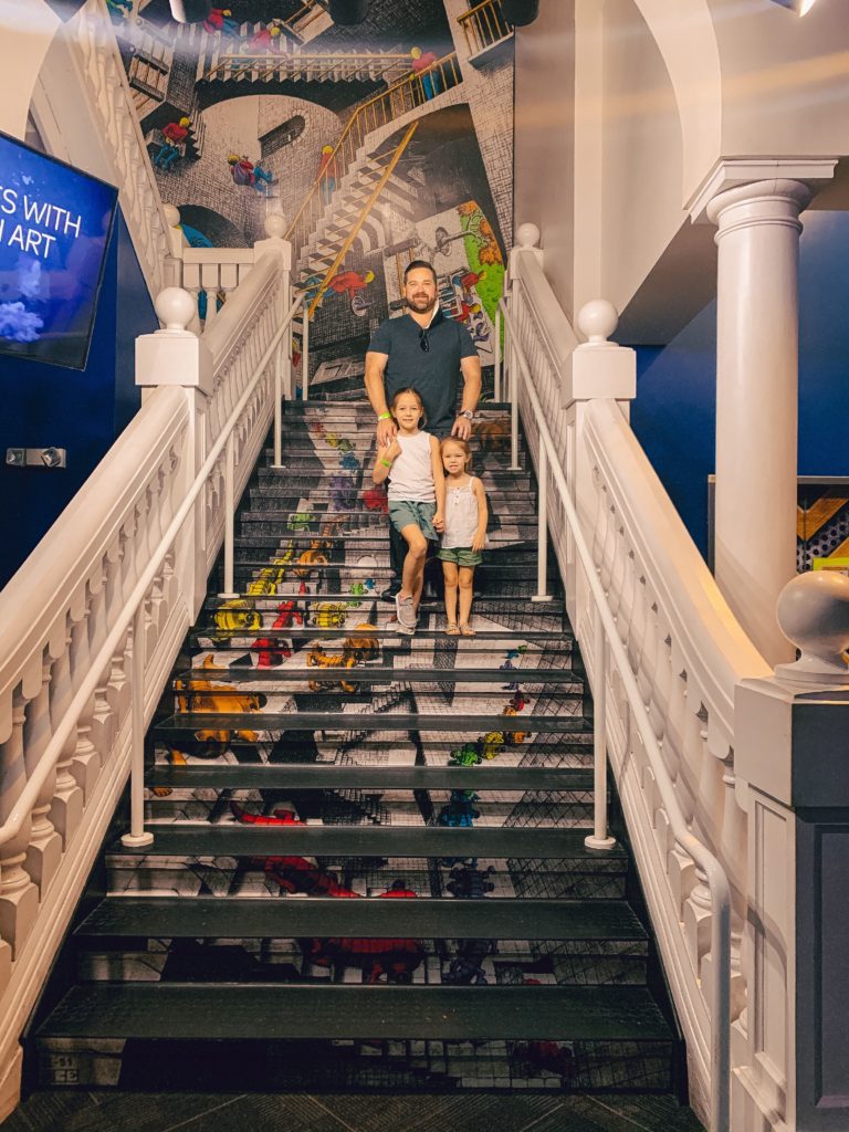 Pigeon Forge TN by popular Nashville travel blog, Nashville Wifestyles: image of a dad and his two young daughters standing on a grand staircase at Wonderworks. 