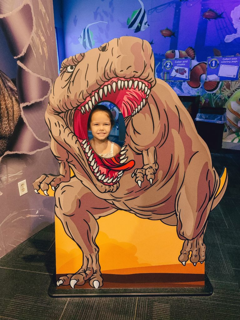 Pigeon Forge TN by popular Nashville travel blog, Nashville Wifestyles: image of a young girl standing behind a dinosaur cutout at Wonderworks. 