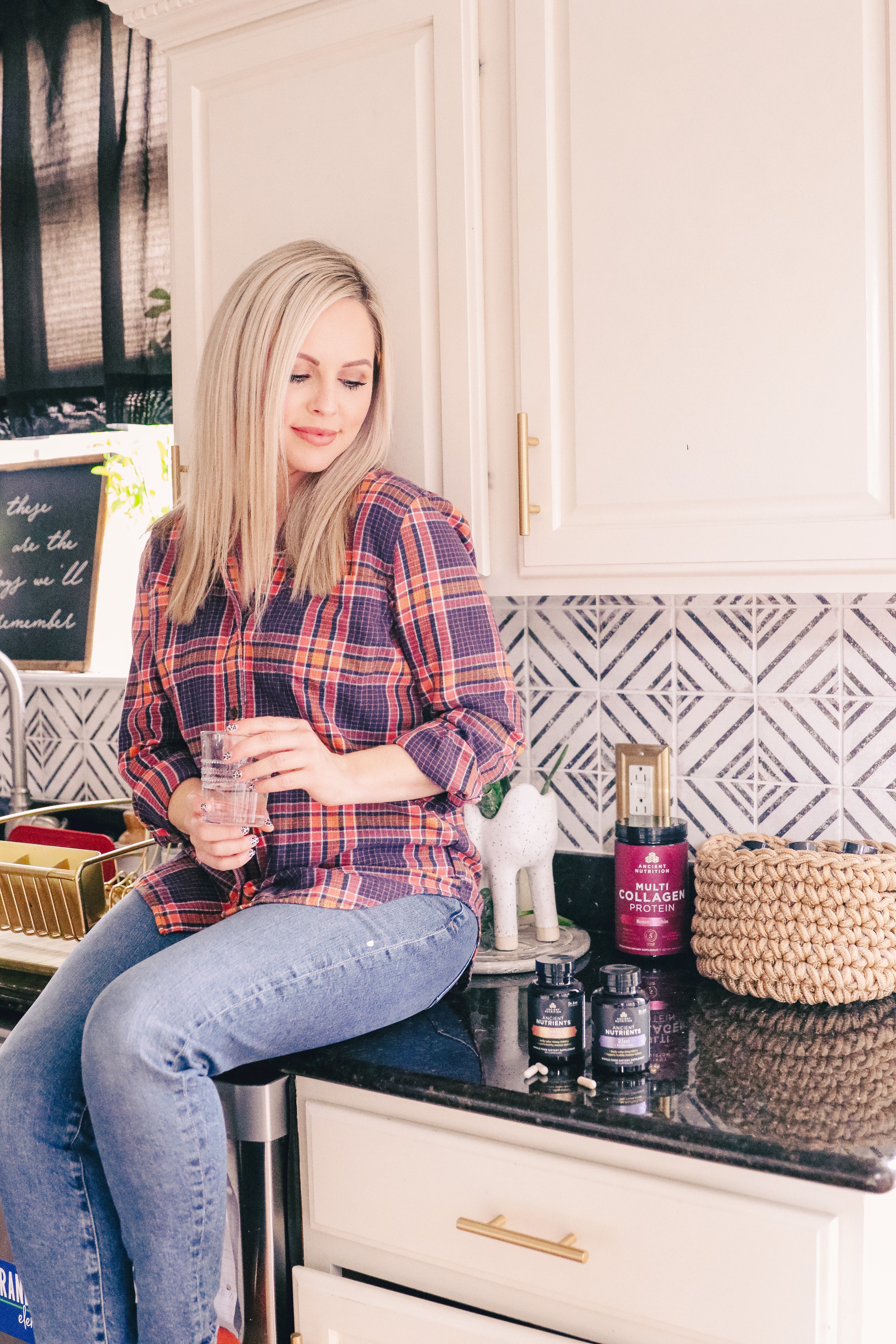 Immune Boosting Supplements by popular Nashville lifestyle blog, Nashville Wifestyles: image of a woman sitting on her kitchen counter next to some Ancient Nutrients bottles.