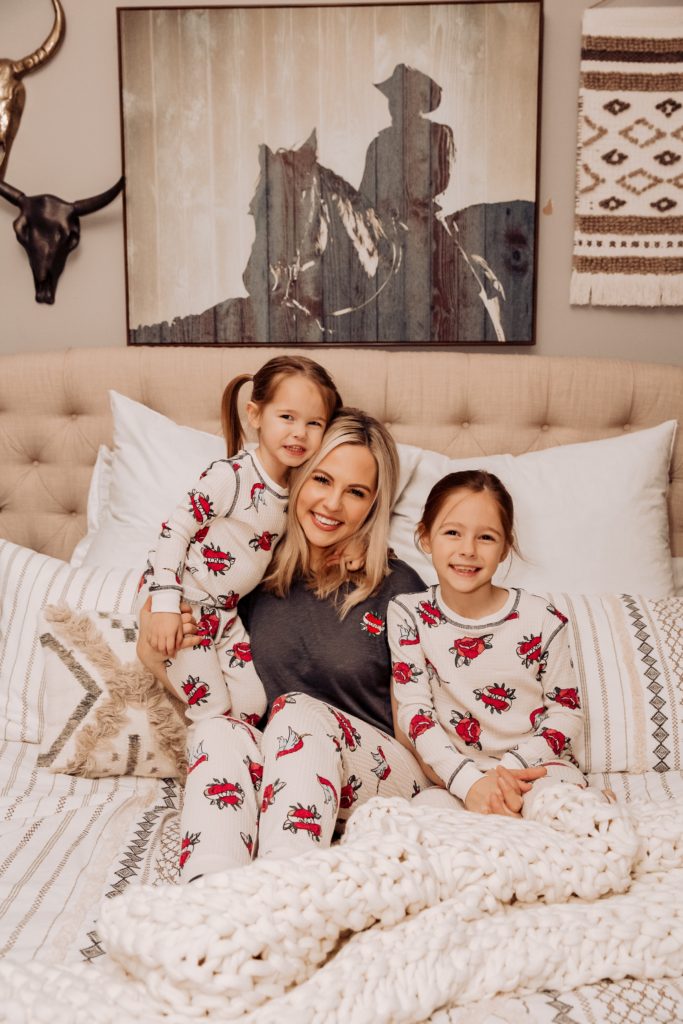 Acts of Kindness by popular Nashville motherhood blog, Nashville Wifestyles: image of two young girls wearing matching flower pajama sets and sitting in bed with their mom. 