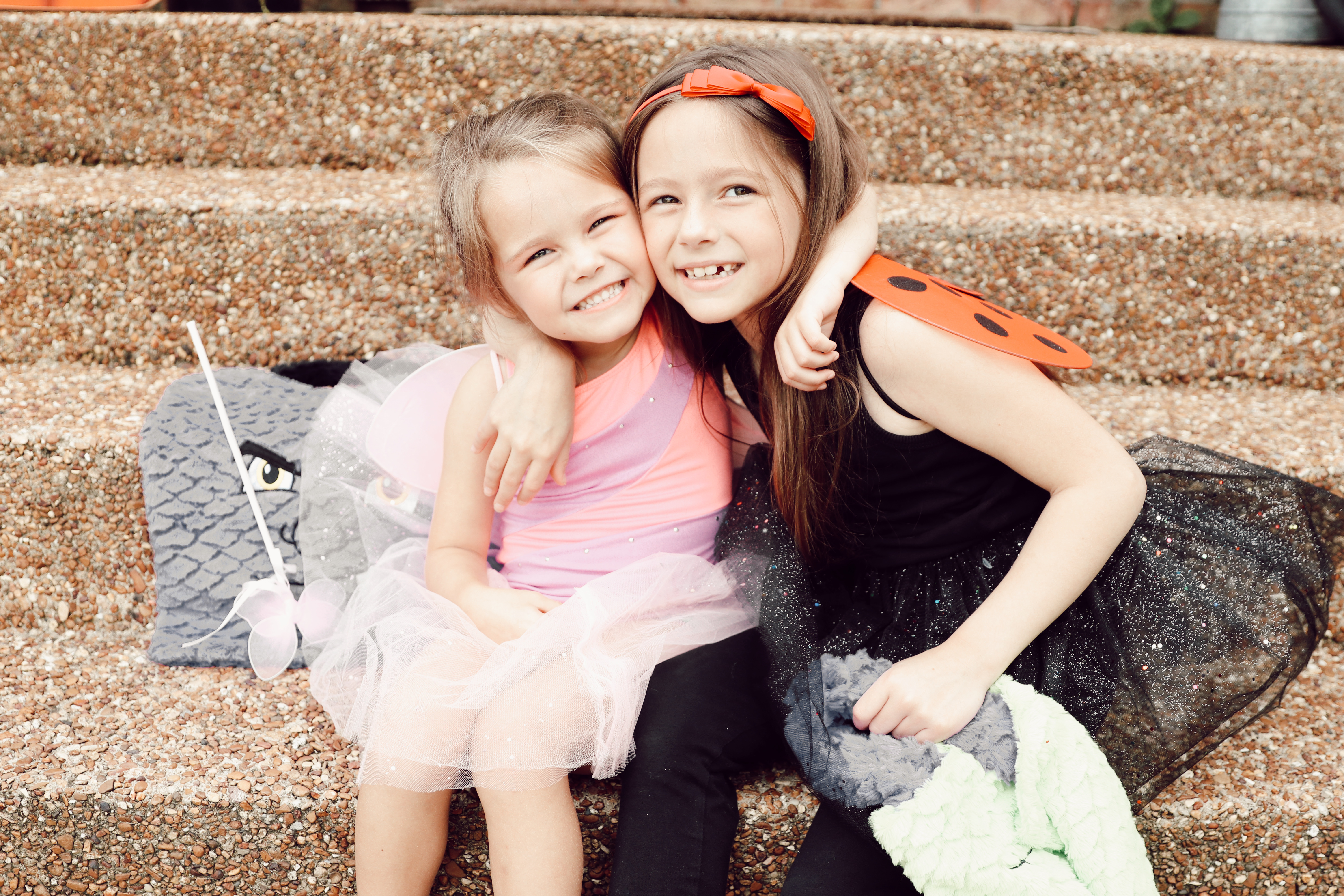 Halloween Activities for Families by popular Nashville lifestyle blog, Nashville Wifestyles: image of two girls dressed up as a butterfly and a ladybug and holding monster face candy bags on their front porch steps.