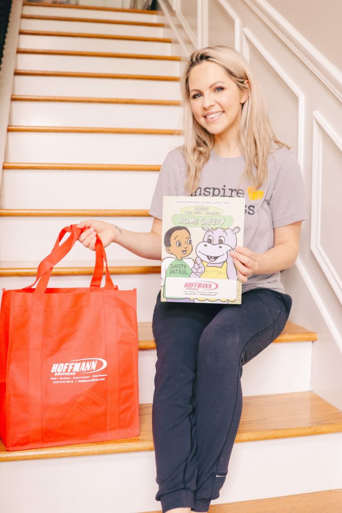 Hoffmann Brothers Home Protection Plan by popular Nashville lifestyle blog, Nashville Wifestyles: image of a woman sitting on her stairs and holding a Hoffmann Brothers home safety book and reusable bag. 
