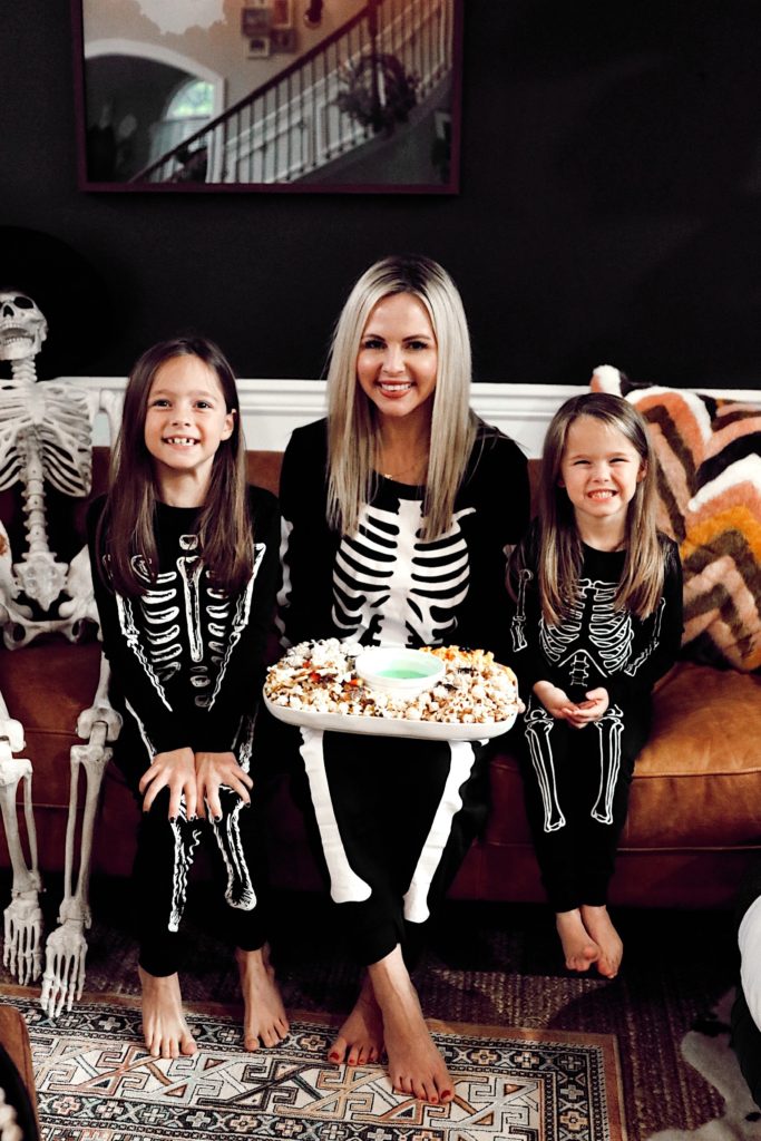 Halloween Snack Ideas by popular Nashville lifestyle blog, Nashville Wifestyles: image of a mom and her two daughters wearing matching skeleton pajamas and holding a popcorn snack tray. 
