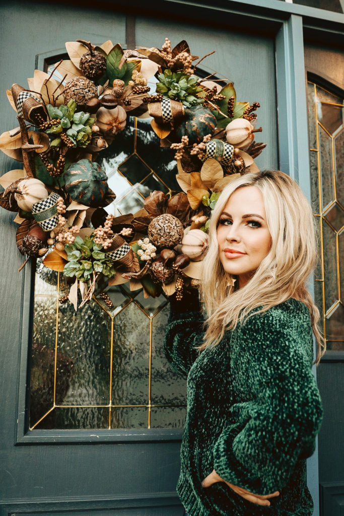 Mackenzie Childs Dishes by popular Nashville life and style blog, Nashville Wifestyles: image of a woman standing next to a Mackenzie Childs fall wreath. 