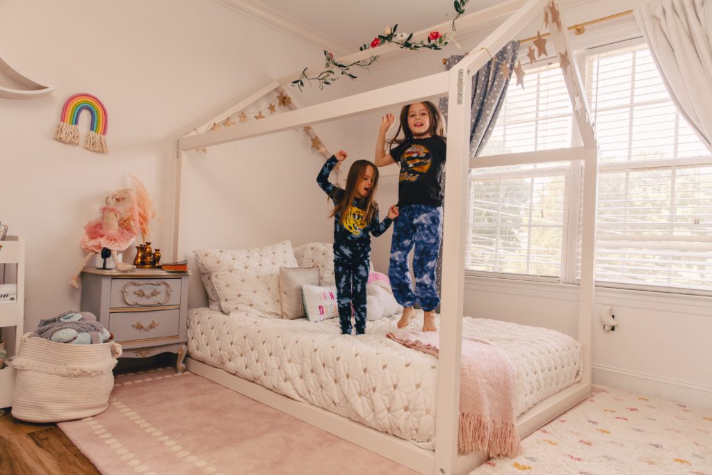 Toddler Floor Bed by popular Nashville motherhood blog, Nashville Wifestyles:  image of two young girls jumping on the mattress in a house frame toddler floor bed. 