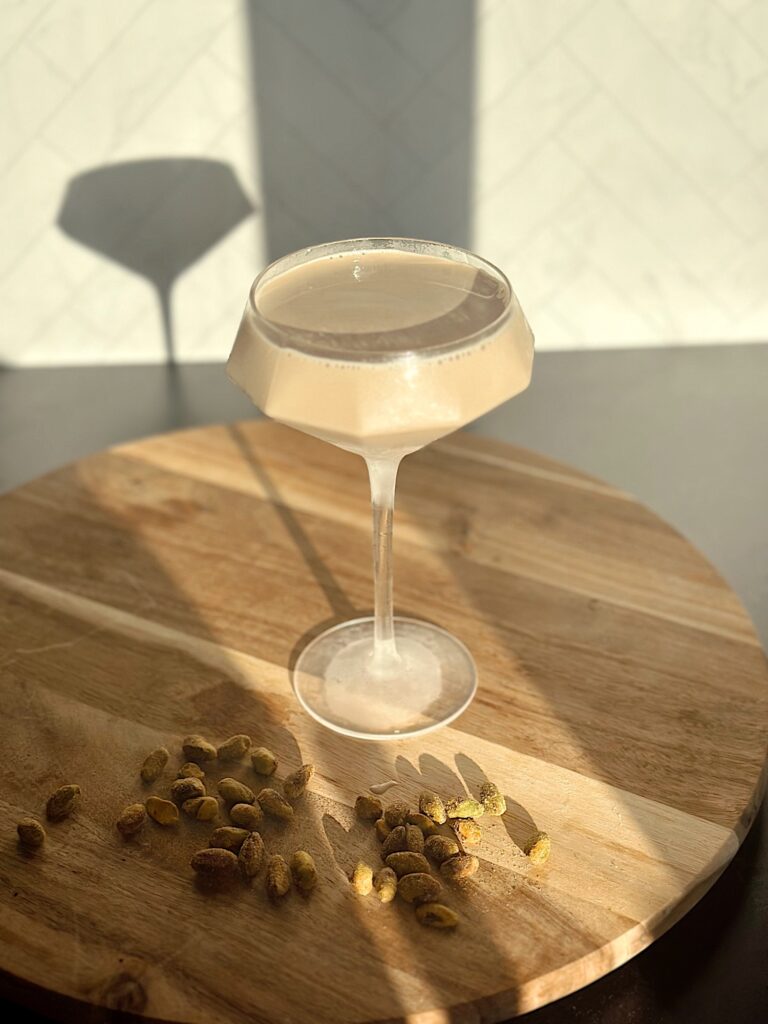 Pistachio Espresso Martini topped with crushed pistachios in a chilled martini glass, creamy coffee cocktail on marble surface with coffee beans and gold shaker nearby