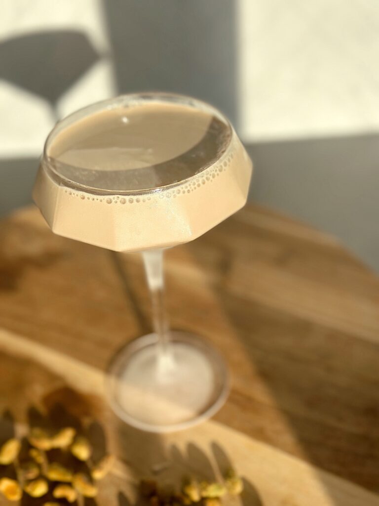 Pistachio Espresso Martini topped with crushed pistachios in a chilled martini glass, creamy coffee cocktail on marble surface with coffee beans and gold shaker nearby