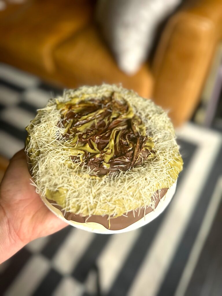 Store-bought cheesecake topped with melted chocolate, pistachio paste, and kataifi in a Dubai chocolate–inspired style.