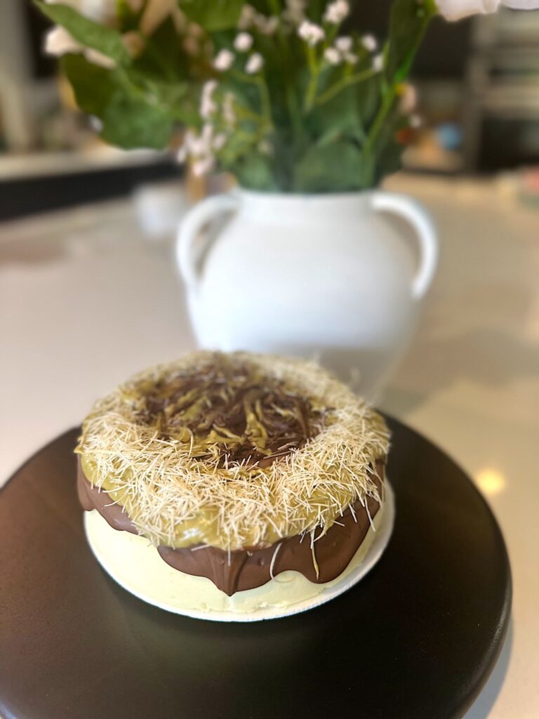 Store-bought cheesecake topped with melted chocolate, pistachio paste, and kataifi in a Dubai chocolate–inspired style.