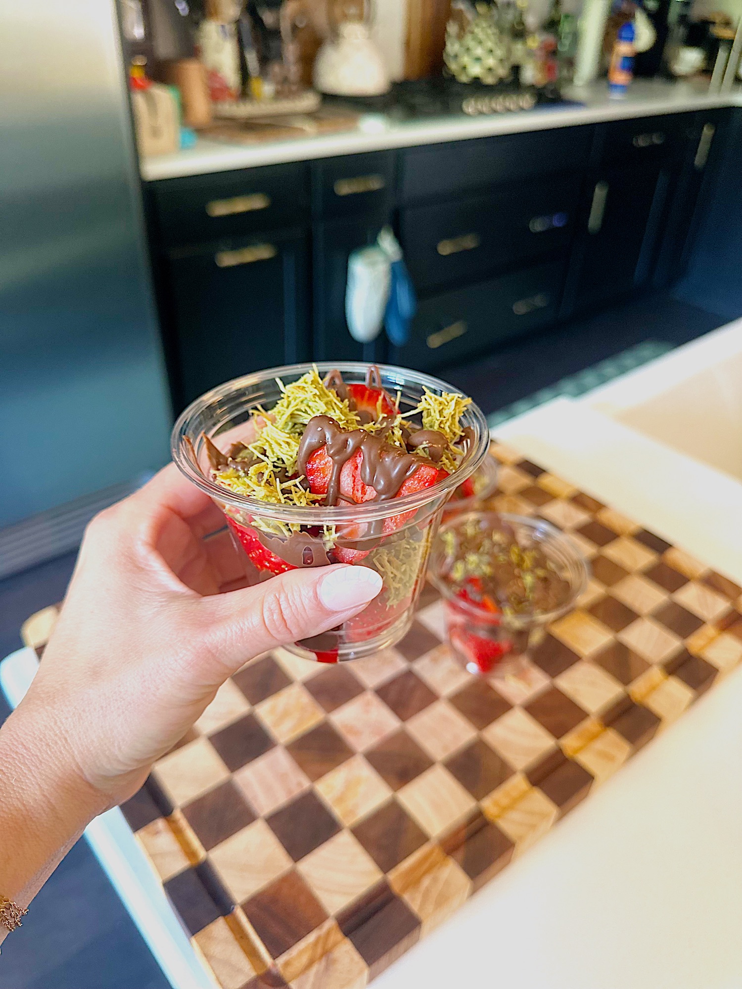 Layered dessert cup with strawberries, pistachio drizzle, kataifi, and chocolate